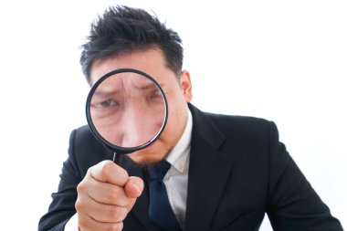 Asyalı işadamı beyaz arka planda izole edilmiş büyüteçten bakıyor