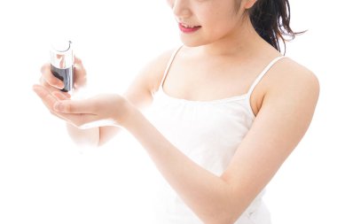 Genç bir kadın beyaz arka planda cildine nemlendirici krem sürüyor.