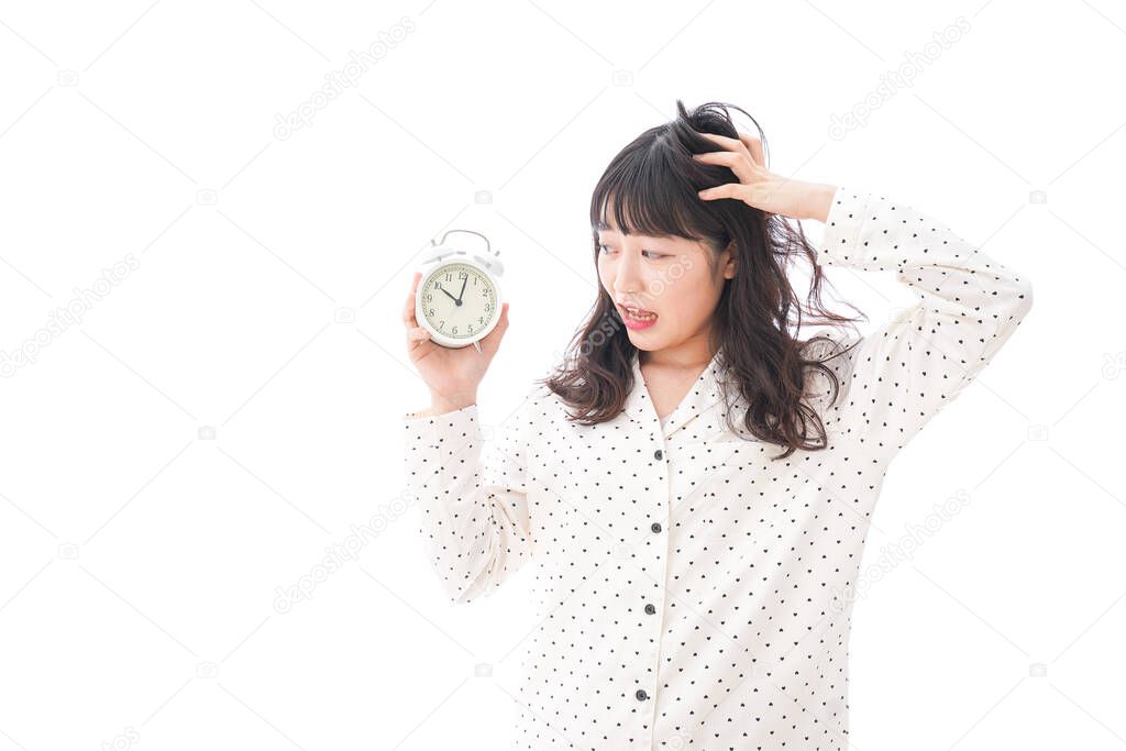 young asian woman in pajamas holding alarm clock isolated on white background