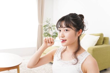 Genç Asyalı kadın evde dişlerini fırçalıyor.