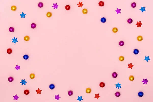 Новогодняя и рождественская рамка. Многоцветные блестящие рождественские украшения - шоколадные конфеты, декоративные звезды и снежинки на розовом бумажном фоне. Вид сверху, плоский, копировальное пространство — стоковое фото