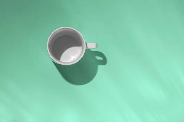 Xícara de chá vazia no fundo de papel de hortelã. Caneca de café de cima. Conceito mínimo Sombra longa com reflexos. Deitado plano, vista superior . — Fotografia de Stock