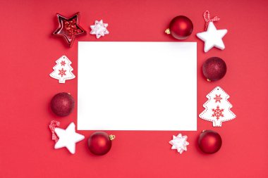 Yeni yıl ve Noel kompozisyonu. Kırmızı arka planda noel süslemeleri olan boş bir kağıt. Üst görünüm, düz görünüm, kopyalama alanı
