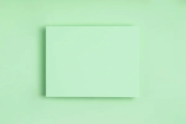 Ελάχιστη γεωμετρική σύνθεση πλαισίου mock up. Λευκό φύλλο λεπτής πράσινης βίβλου σε πράσινο φόντο. Πρότυπο σχεδιαστική κάρτα πρόσκληση. Πάνω άποψη, επίπεδη lay, αντίγραφο χώρου. Οριζόντια κατεύθυνση. — Φωτογραφία Αρχείου