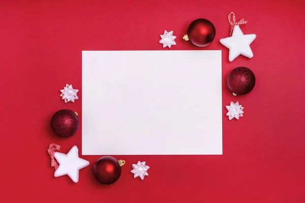 Yeni yıl ve Noel kompozisyonu. Kırmızı arka planda noel süslemeleri olan boş bir kağıt. Üst görünüm, düz görünüm, kopyalama alanı