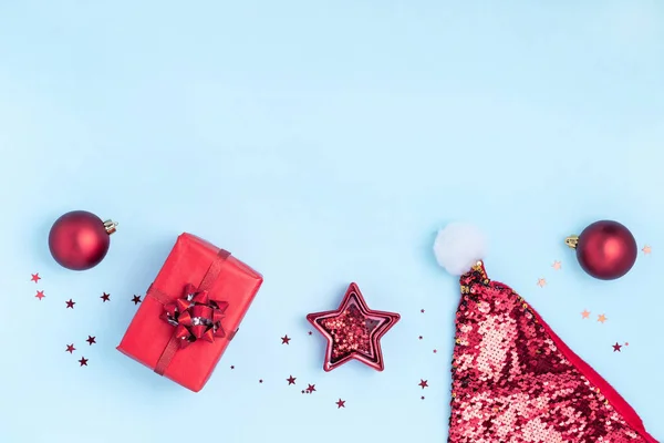 Yeni yıl ve Noel kompozisyonu. Kırmızı toplar, kırmızı yıldız, hediye kutuları, pastel mavi arka planda Noel Baba 'nın şapkası ve parıltıları. Üst görünüm, düz görünüm, kopyalama alanı