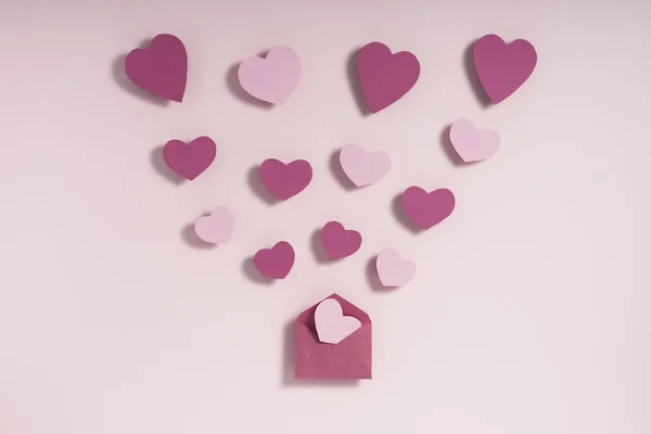 Валентинів день композиції. Рожеві та фіолетові серця дують з конверта на рожевому тлі. Літературна концепція — стокове фото
