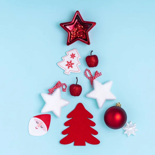 Año Nuevo y composición navideña en forma de árbol de Navidad. Decoraciones rojas y blancas: estrellas, bolas de Navidad, juguetes sobre fondo de papel azul pastel. Vista superior, plano, espacio para copiar —  Fotos de Stock