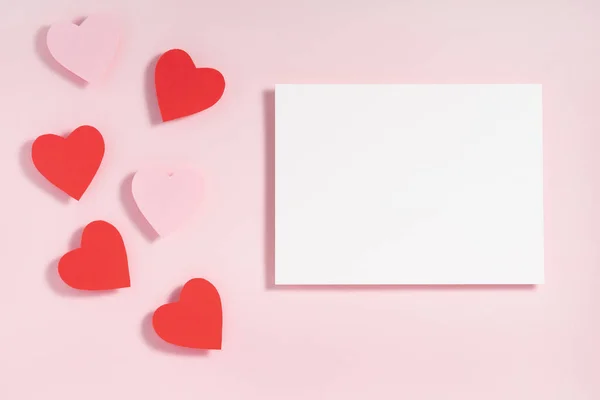 Sevgililer Günü kompozisyonu. Kırmızı pembe kalpler, pastel pembe arka planda boş kağıtlar. Üst görünüm, düz görünüm, kopyalama alanı