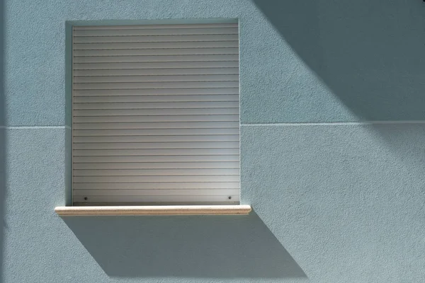 Duvarında güneşin gölgesi olan minimalist mavi pencere. Evin yan duvarında asılı bir kare mavi pencere.