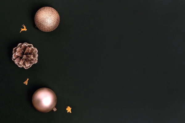 Nieuwjaars- en kerstkaart. Gouden kerstversiering - glanzende ballen, dennenappels op zwarte achtergrond. Bovenaanzicht, flat lay, kopieerruimte — Stockfoto