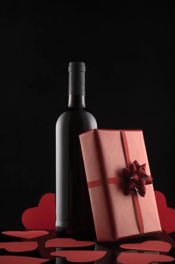 Hediye kutusu, şarap şişesi ve siyah arka planda kırmızı kalpler..