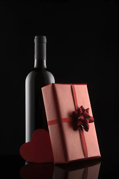 Gift box, wine bottle and red hearts on black background. — Stock Photo, Image