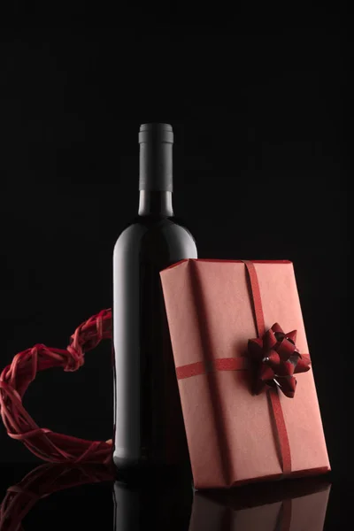 Gift box, wine bottle and red hearts on black background.