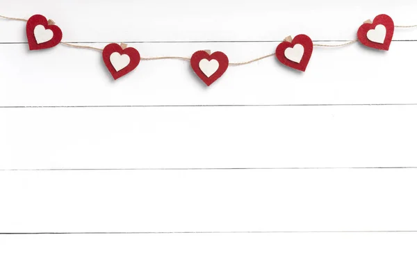 Espinhos de roupa com corações vermelhos pendurados na corda atrás da superfície de madeira branca . Fotografias De Stock Royalty-Free
