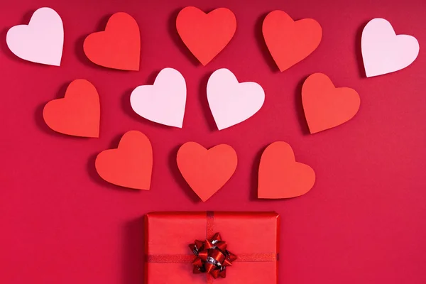 Gift box and valentine hearts on red surface. Top view, flat lay