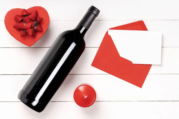 Heart, candle, wine bottle on white wooden surface.
