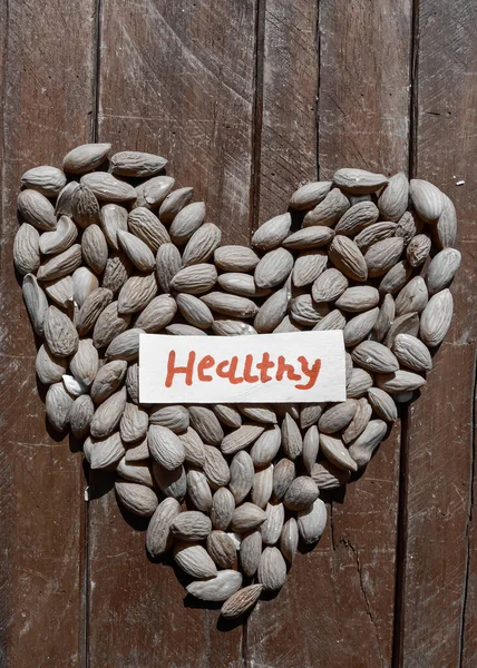text writing healthy ,healthy text writing on almond nuts beautiful view,dry almond on wooden, kernel nut heart shape wooden table,fresh hazelnut  top view,highly protein nuts hearts shape