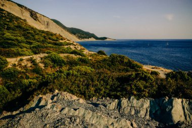 Mountainous rocky seashore covered with juniper forest in summer. A steep cape with an adjacent quiet bay and a stone beach. View of the Utrish Reserve, Cape Crocodile. clipart