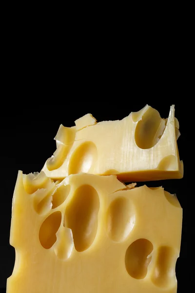 Um pedaço de queijo suíço com grandes buracos em um fundo preto com reflexão. estilo minimalista de arte alimentar. closeup de queijo — Fotografia de Stock