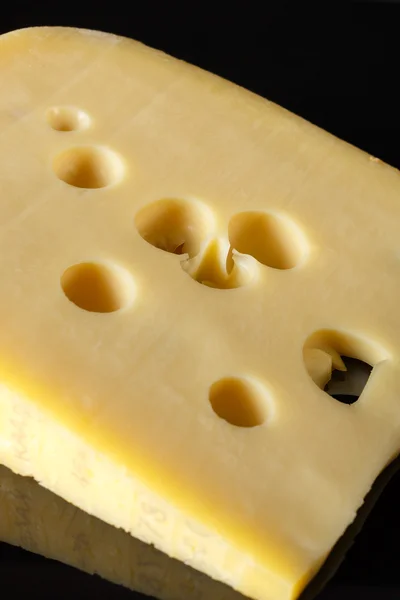 Um pedaço de queijo suíço com grandes buracos em um fundo preto com reflexão. estilo minimalista de arte alimentar. closeup de queijo — Fotografia de Stock