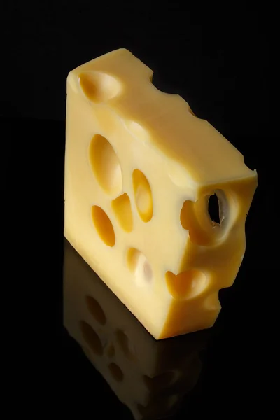 Кусочек швейцарского сыра с большими отверстиями на черном фоне с отражением. минималистский стиль искусства питания. Сыр подорожал — стоковое фото