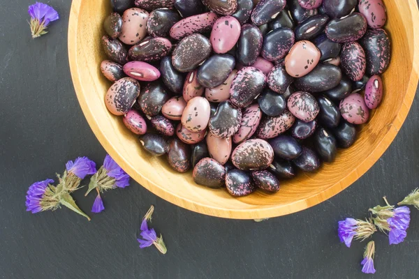 grain purple beans of different colors in a wooden bowl on a black background. vegetarian raw food. food color background