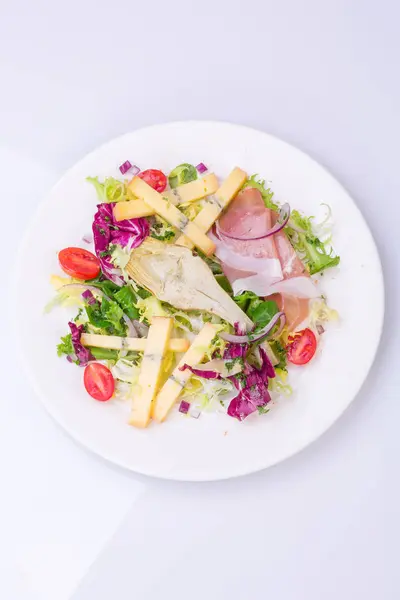 新鮮な野菜と白い皿にチーズのミックス サラダ。ミニトマトのサラダ、レタス、マリネ、アーティ チョーク、タマネギ、チーズ、ハム — ストック写真