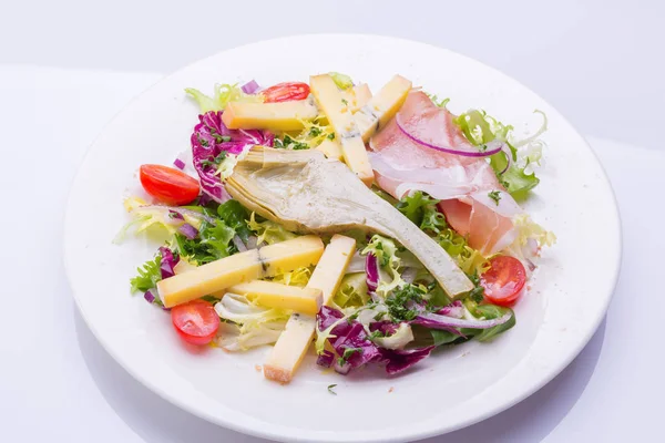 Dans une assiette blanche, mélanger la salade avec les légumes frais et le fromage. salade de tomates cerises, laitue, artichaut mariné, oignon, fromage, jambon — Photo