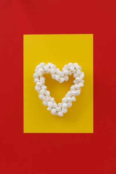 Coroa de conchas brancas na forma de um coração em um papel de fundo amarelo-vermelho. Conceito ainda minimalista de amor, sentimentos, felicidade — Fotografia de Stock