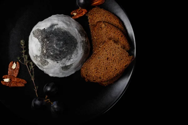 Queso de cabra con moho en forma de pirámide con frutos secos y uvas en un plato negro. Una instantánea de comida en un piso bajo . — Foto de Stock