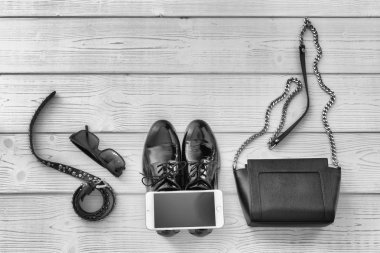 Bir kemer, gözlük, çanta, telefon ve iş ayakkabıları görünümü yukarıdan zarif kümesi. Moda ayakkabı ve aksesuarları ile metin için ahşap arka plan görüntüsü. Siyah beyaz resim moda aksesuarları.
