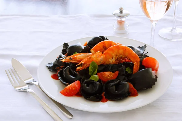 İtalyan Mantısı ile mürekkep mürekkep balığı, domates, beyaz bir tabak karides. Masaya yemek