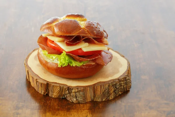 Un sándwich casero con jamón, queso, ensalada, tomate y bollo salado en una mesa de madera marrón . — Foto de Stock