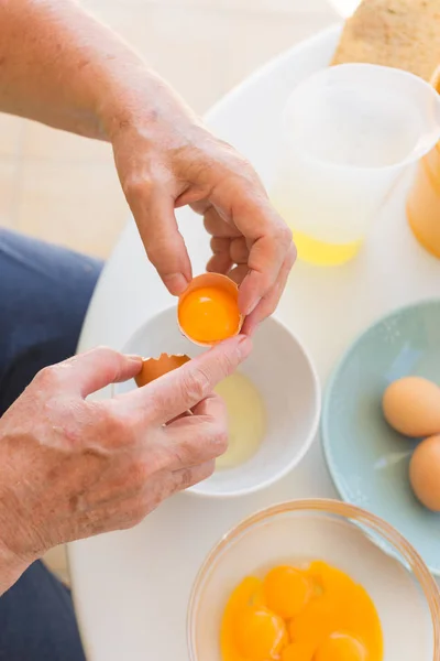Разбитые яйца. Женские руки разбивают яйца на заднем столе с посудой — стоковое фото