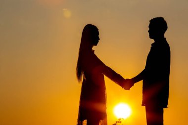 Gün batımında el ele tutuşan aşıkların silueti.,