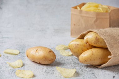 Gri zemindeki çuvallardan patatesler dökülüyor.