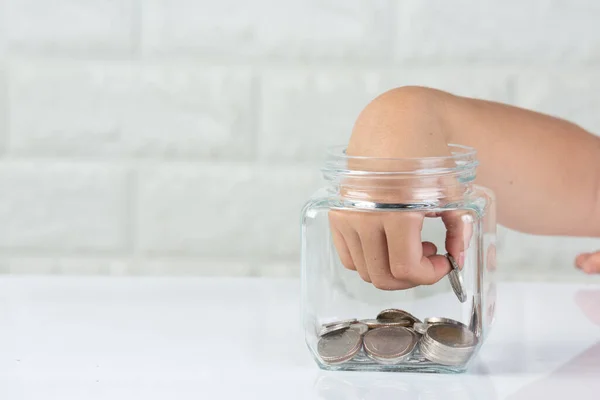 kid drop coin in to the jar on white background in front of white wall