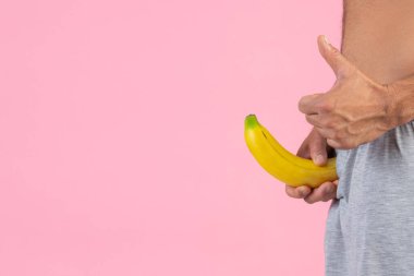 Elinde pembe arka planda muz tutan ayakta duran bir adam.