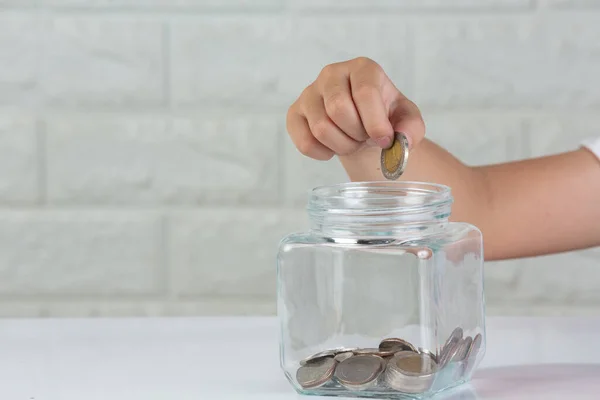 kid drop coin in to the jar on white background in front of white wall