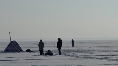 Kış. Çocuklu bir aile balıkçıların çadırının yanındaki donmuş Ob nehrinin buzunda duruyor. Çevredeki akıllı telefonuyla fotoğraf çeken bir kadın. Sibirya 'da. Arka ışıklandırma.