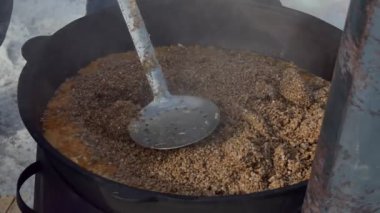 Basit bir yemek. Aşçı karabuğday lapasıyla tavuk etini ve baharatları evin dışındaki fırında büyük bir tencerede karıştırıyor. Kapatın. Sibirya.
