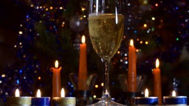 Tatiller, Noel, yeni yıl. Mumların ve yanıp sönen renkli ışıkların arka planında duran bardağa bir şampanya akıntısı dökülüyor. Kapat..