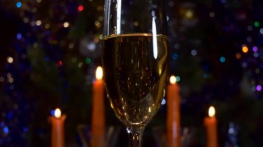 Noel, yeni yıl. Bir bardak şampanya, arka planda mumlar ve yanıp sönen renkli ışıkların karşısında duruyor. Kapat..