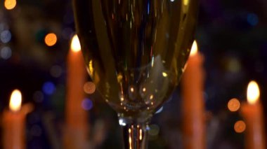 Noel, yeni yıl. Bir bardak şampanya, arka planda mumlar ve yanıp sönen renkli ışıkların karşısında duruyor. Kapat..