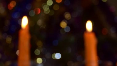 Noel, yeni yıl. Arka plan videosu. Yanan iki mum, Noel ağacının renkli parıldayan ışıklarının arka planında duruyor. Odaklanamıyorum. Kapat..