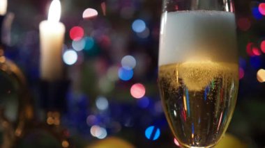 Noel, yeni yıl, tatiller. Şampanya bardağındaki baloncuklar mumların ve yanıp sönen renkli ışıkların arka planına karşı. Arka plan videosu. Kapat..