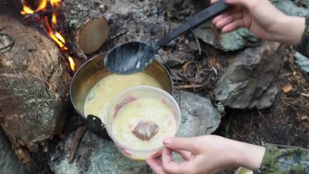 自然の中で冒険 若い女性が火で調理されたシンプルな食べ物のプレートに注ぐ シベリア — ストック動画