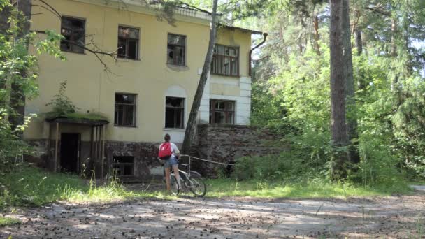 Паранормальное Место Молодая Женщина Велосипедистка Осматривает Старые Разрушенные Здания Лесу — стоковое видео