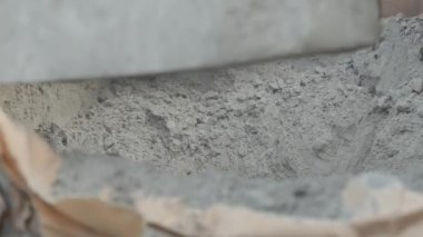 Adam torbadaki kuru çimentoyu bir malayla kovaya döküyor.